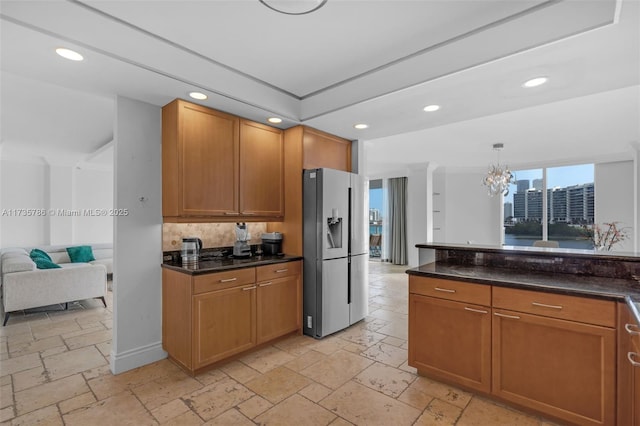 kitchen with decorative light fixtures, dark stone countertops, stainless steel fridge, decorative backsplash, and an inviting chandelier