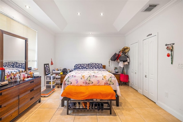 bedroom with light tile patterned floors, a raised ceiling, and multiple closets