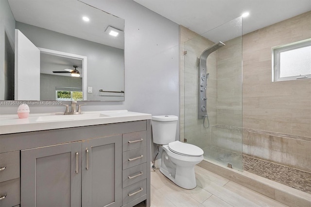 bathroom with a healthy amount of sunlight, tiled shower, vanity, and toilet