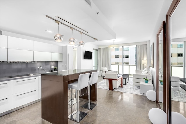 kitchen featuring a kitchen island, a breakfast bar area, white cabinets, hanging light fixtures, and black electric stovetop