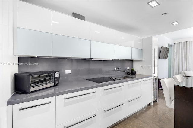 kitchen with white cabinetry, black electric cooktop, sink, and backsplash