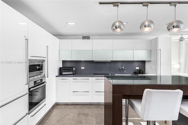 kitchen featuring hanging light fixtures, backsplash, stainless steel appliances, and white cabinets