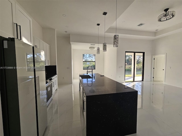 kitchen featuring sink, a kitchen island with sink, white cabinetry, dark stone countertops, and fridge