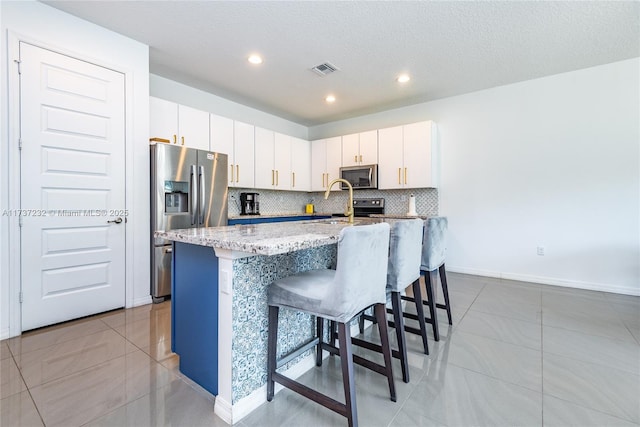 kitchen featuring appliances with stainless steel finishes, a kitchen breakfast bar, a kitchen island with sink, decorative backsplash, and white cabinets