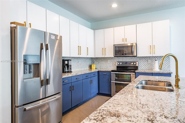 kitchen with blue cabinets, sink, appliances with stainless steel finishes, light stone countertops, and white cabinets