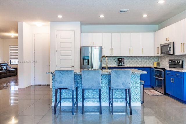 kitchen with blue cabinets, a breakfast bar area, stainless steel appliances, a kitchen island with sink, and white cabinets