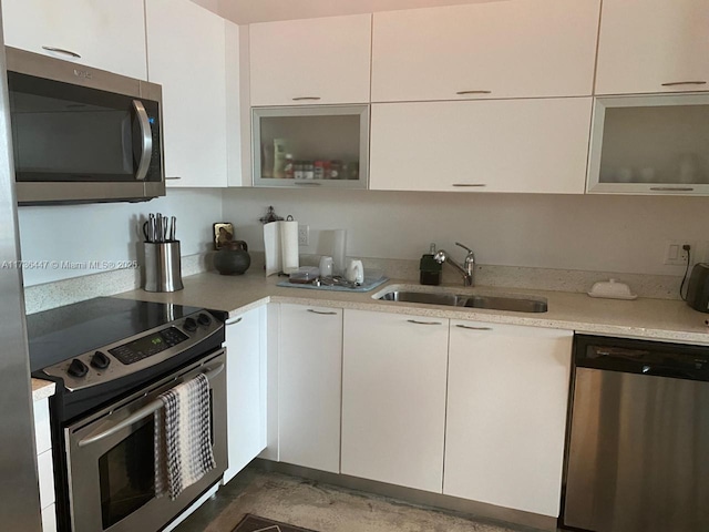 kitchen with white cabinets, a sink, light countertops, stainless steel appliances, and glass insert cabinets