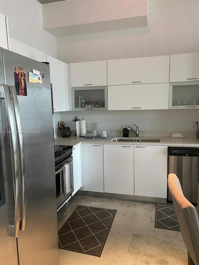 kitchen featuring white cabinets, light stone counters, appliances with stainless steel finishes, concrete flooring, and a sink