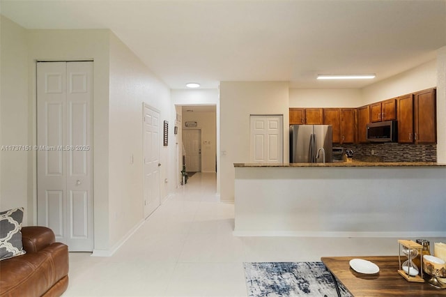 kitchen with appliances with stainless steel finishes, kitchen peninsula, light tile patterned floors, and backsplash