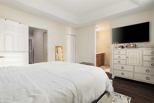 bedroom with a raised ceiling, ensuite bathroom, and dark wood-type flooring