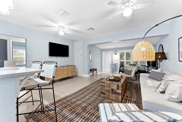 living area featuring a ceiling fan, visible vents, baseboards, and light tile patterned floors