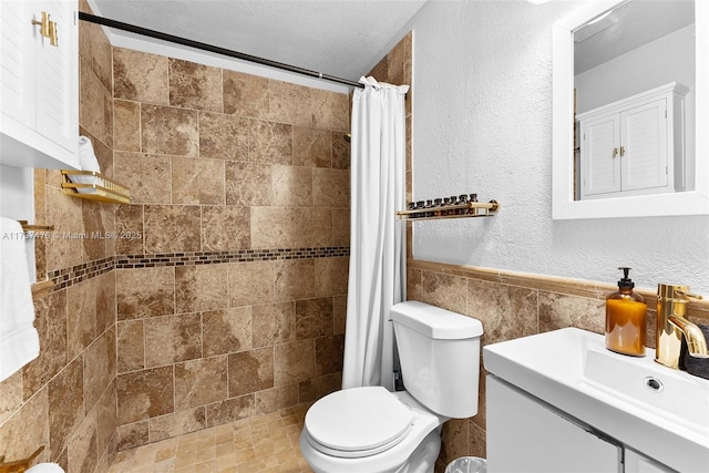 full bath with a textured wall, toilet, vanity, tile walls, and a tile shower