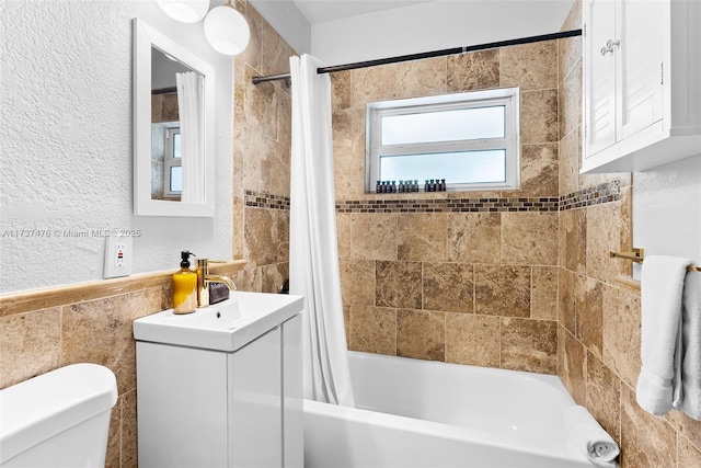 full bathroom with a textured wall, shower / tub combo with curtain, vanity, and toilet