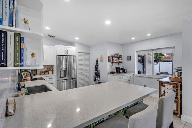 kitchen featuring sink, stainless steel fridge, white cabinets, light tile patterned flooring, and decorative backsplash