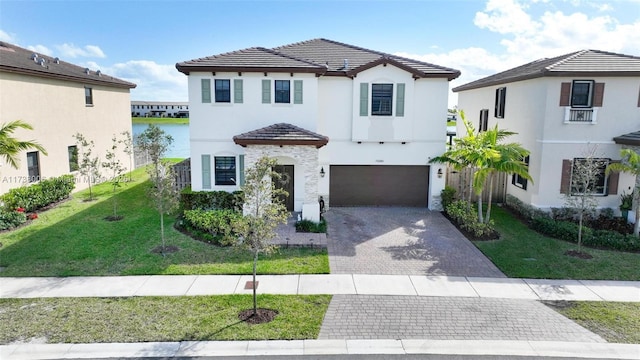 view of front of home featuring decorative driveway, a tile roof, a water view, an attached garage, and a front lawn