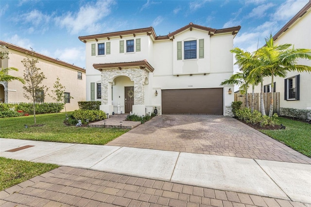 mediterranean / spanish home featuring fence, stone siding, decorative driveway, stucco siding, and a front yard