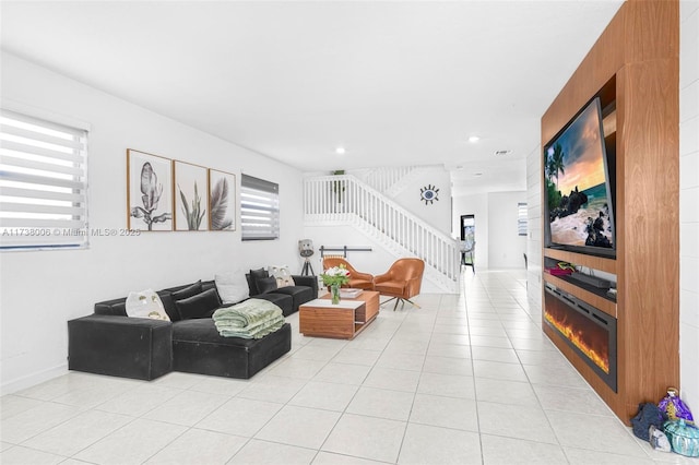 living room with light tile patterned floors, stairway, a glass covered fireplace, and a healthy amount of sunlight