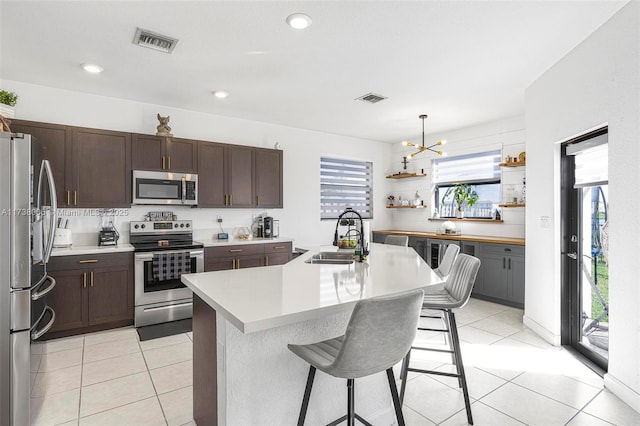 kitchen featuring a breakfast bar, a center island with sink, light countertops, visible vents, and appliances with stainless steel finishes