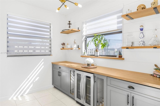 kitchen with light tile patterned floors, beverage cooler, butcher block counters, gray cabinets, and open shelves