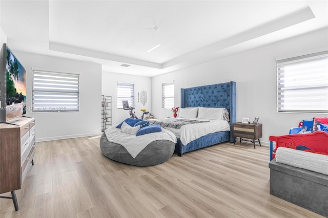 bedroom featuring light wood finished floors, a raised ceiling, and baseboards