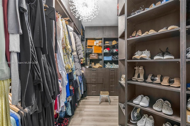 spacious closet with light wood-type flooring and a chandelier