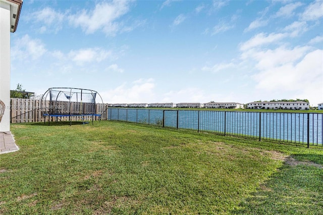 view of yard featuring a water view, a fenced backyard, and a trampoline