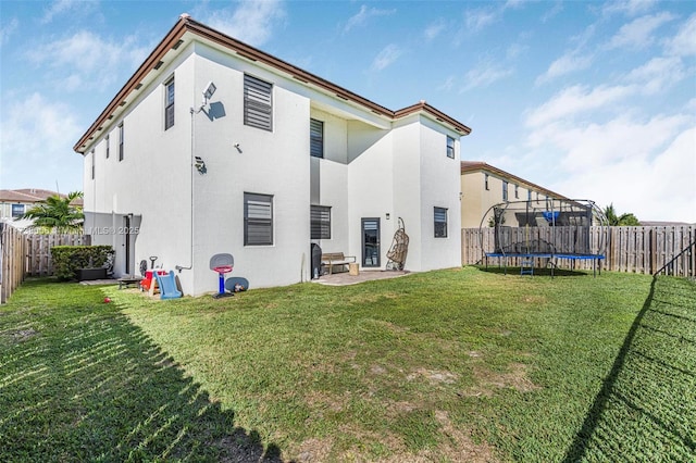 rear view of property with a trampoline, a fenced backyard, and a yard