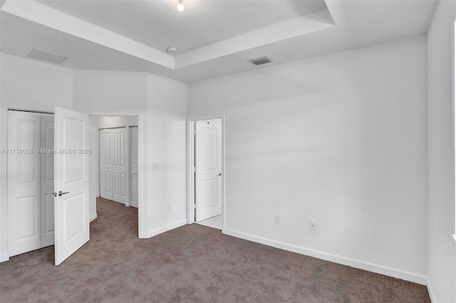 unfurnished bedroom featuring a raised ceiling and dark colored carpet