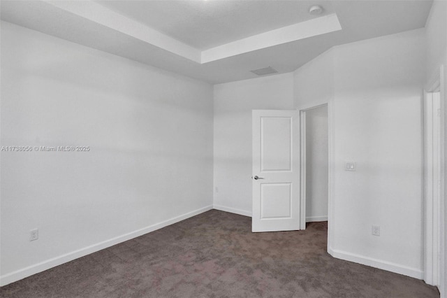 unfurnished room with a tray ceiling and dark carpet