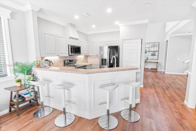 kitchen featuring ornamental molding, light wood-type flooring, light countertops, backsplash, and stainless steel appliances