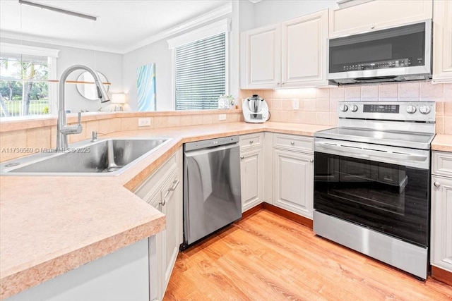 kitchen with backsplash, appliances with stainless steel finishes, a sink, ornamental molding, and light wood-style flooring