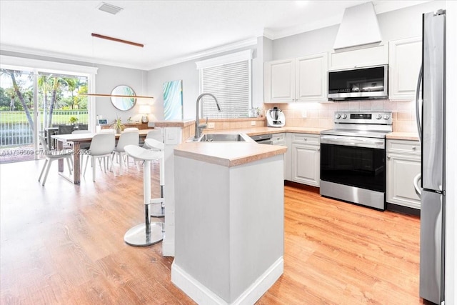 kitchen with a peninsula, appliances with stainless steel finishes, ornamental molding, and a sink