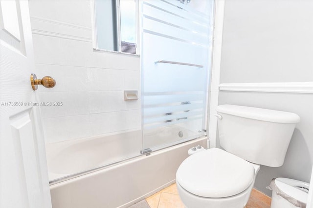 bathroom featuring tile patterned flooring, toilet, and shower / bath combination with glass door