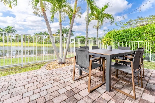 view of patio with fence, outdoor dining area, and a water view