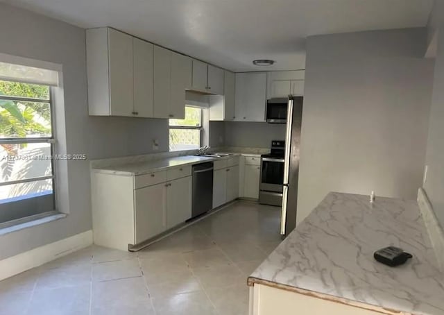 kitchen with appliances with stainless steel finishes, sink, light tile patterned floors, and white cabinets