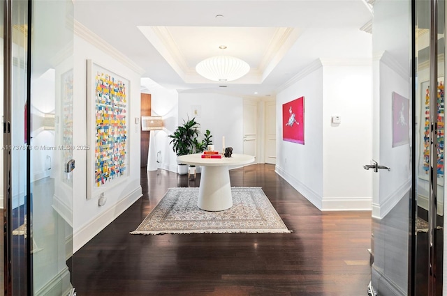 interior space with baseboards, a raised ceiling, dark wood-style flooring, and crown molding