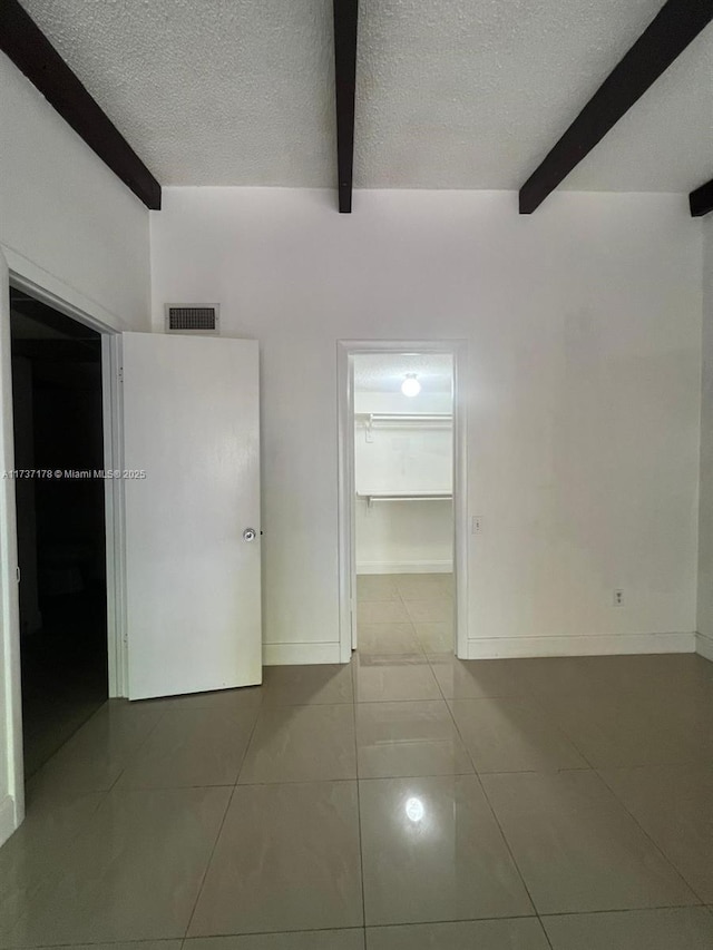 tiled spare room featuring beam ceiling and a textured ceiling