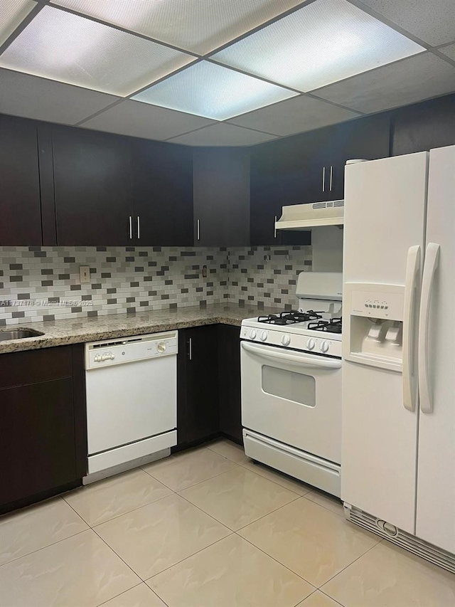 kitchen featuring tasteful backsplash, light stone countertops, a drop ceiling, and white appliances