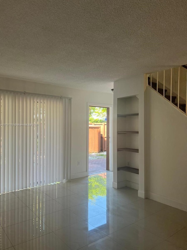 unfurnished room featuring light tile patterned floors, a textured ceiling, and built in shelves