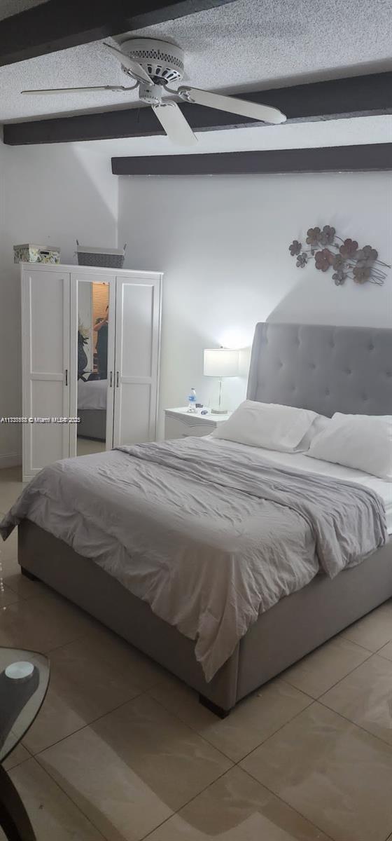 tiled bedroom with beamed ceiling, ceiling fan, and a textured ceiling