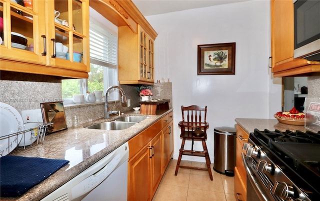 kitchen with light tile patterned floors, light stone counters, stainless steel appliances, a sink, and tasteful backsplash