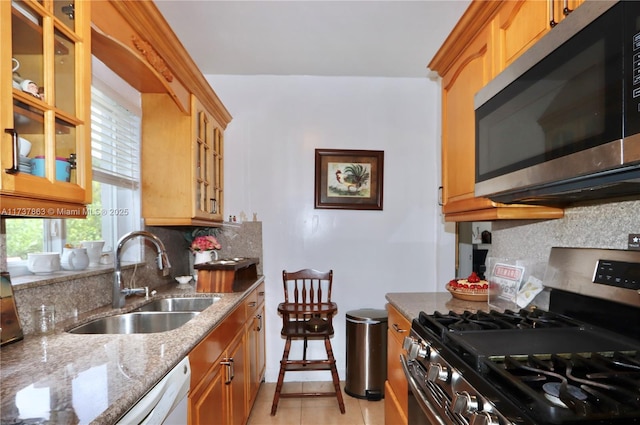 kitchen with backsplash, appliances with stainless steel finishes, light stone counters, and a sink