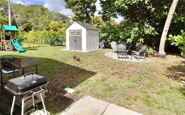 view of yard featuring an outdoor fire pit, a playground, an outdoor structure, fence, and a shed