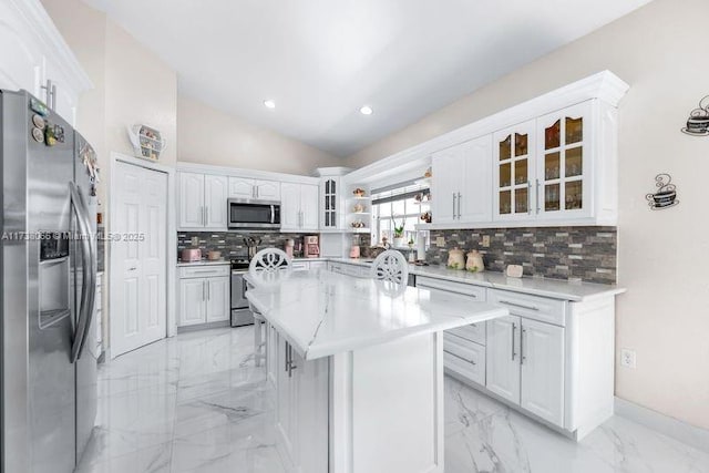 kitchen featuring lofted ceiling, appliances with stainless steel finishes, white cabinetry, tasteful backsplash, and a kitchen island