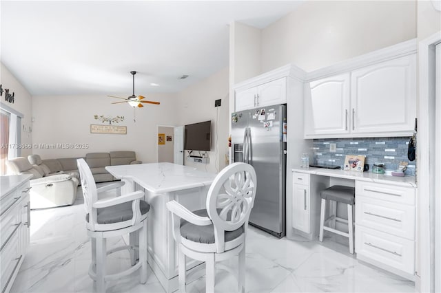 kitchen with ceiling fan, white cabinetry, backsplash, a kitchen bar, and stainless steel fridge with ice dispenser