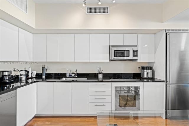 kitchen featuring stainless steel appliances, rail lighting, sink, and white cabinets