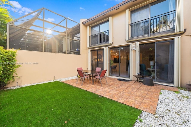 rear view of property featuring a yard, glass enclosure, and a patio area