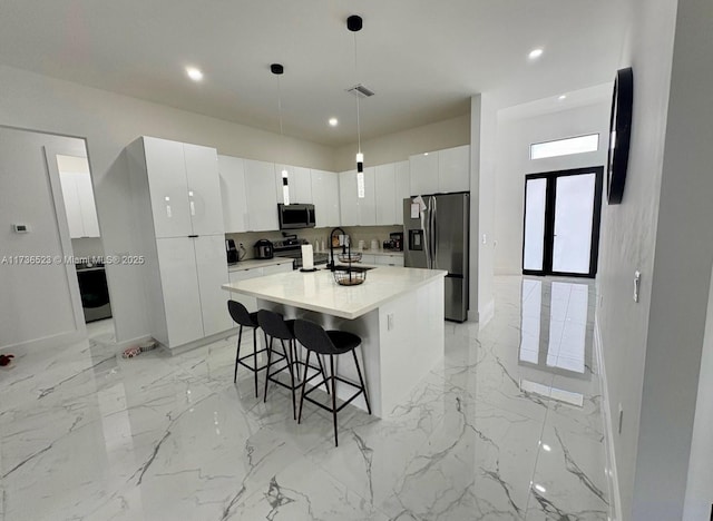 kitchen featuring decorative light fixtures, a kitchen breakfast bar, stainless steel appliances, a kitchen island with sink, and white cabinets