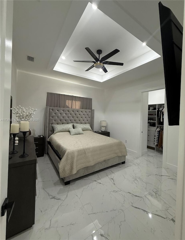 bedroom with ceiling fan, a tray ceiling, and a spacious closet