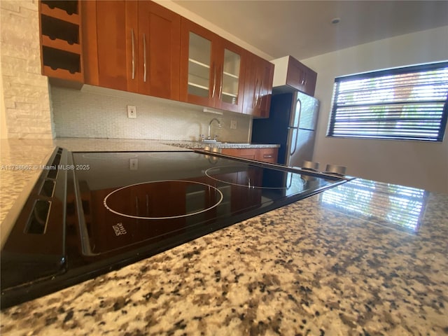 kitchen with sink, stainless steel fridge, decorative backsplash, stove, and light stone counters